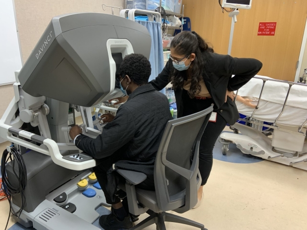 Dr. Barnabas Alayande (left) tries out the DaVinci Robot backpack with the help of General Surgery Resident and Surgical Education Fellow Dr. Ananya Anand